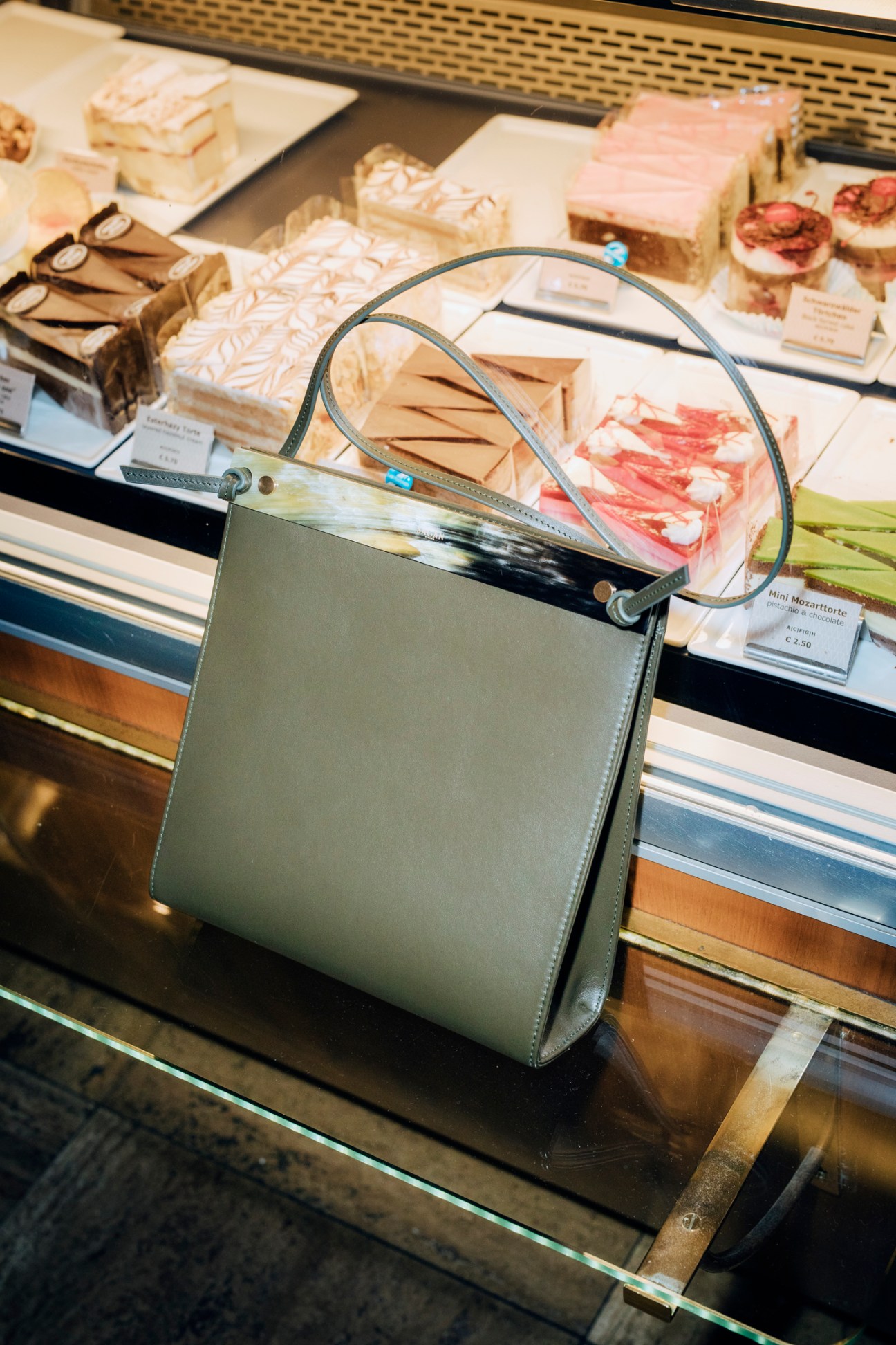 Olive green leather handbag by Sagan Vienna displayed on glass surface in front of cheese counter