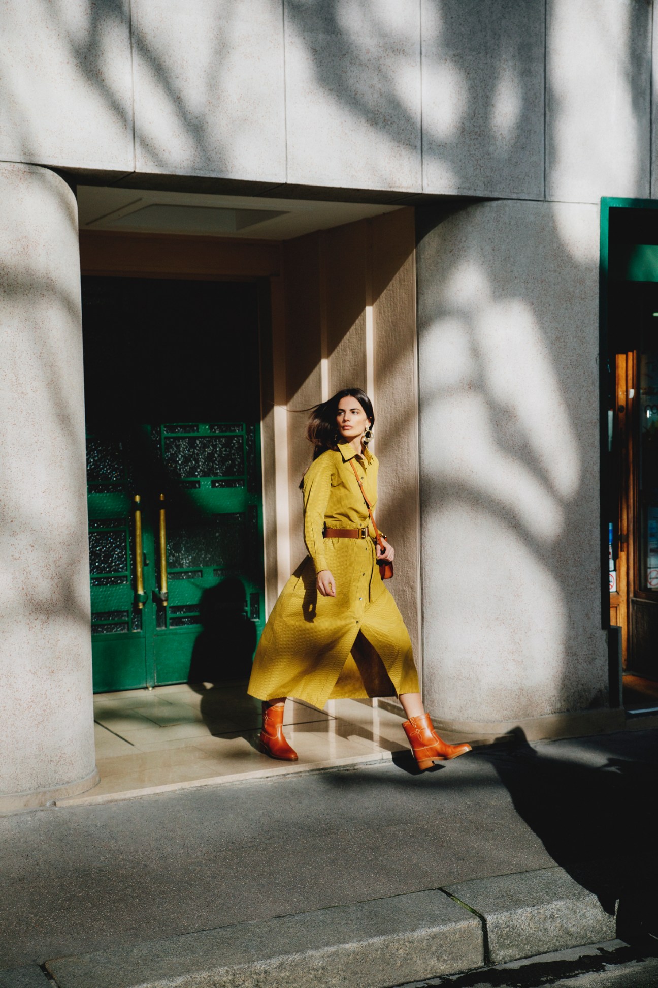 Woman in yellow dress and brown belt walking in modern architectural space with dramatic shadows