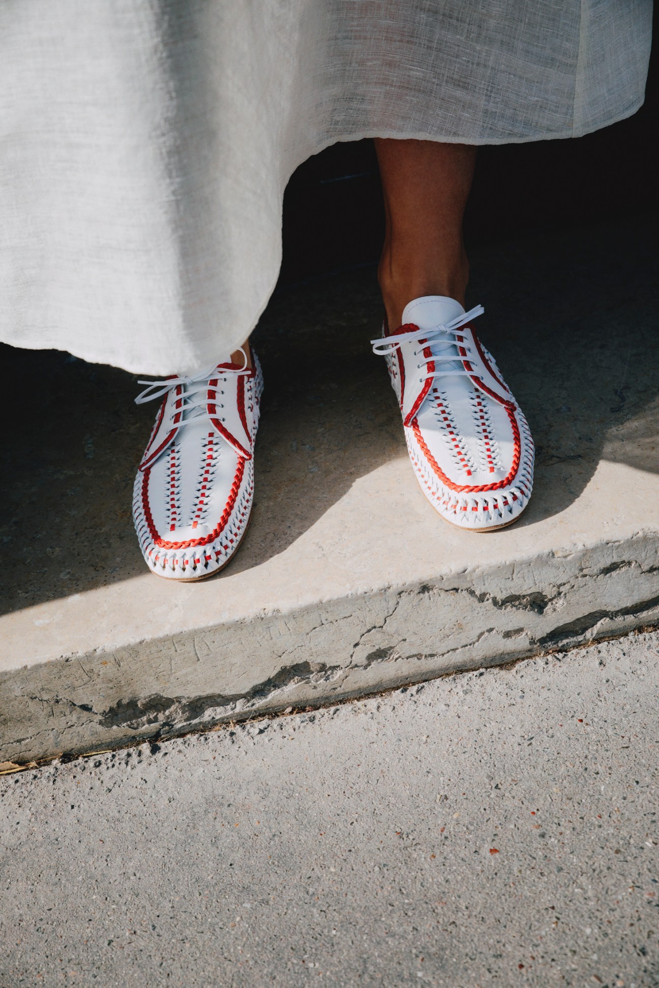 Person wearing white shoes with red stitching and a grey skirt standing on concrete