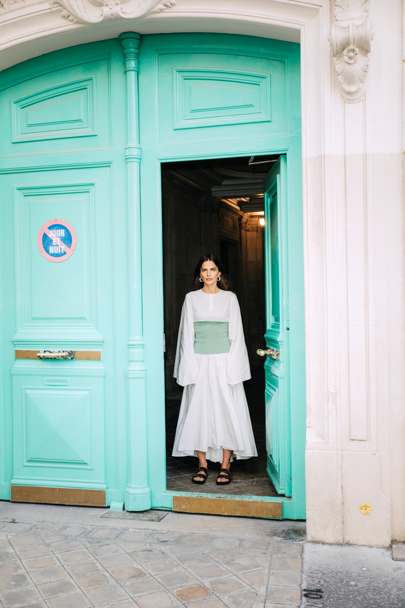 Woman in white Loewe dress with green square detail standing in turquoise doorway in Paris