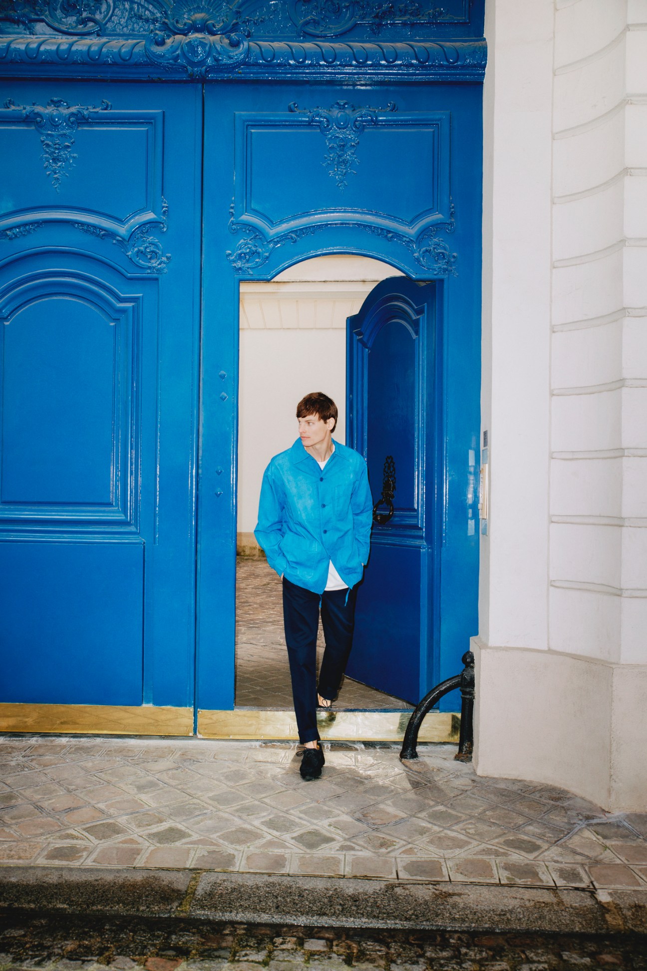 Young man in blue jacket standing in ornate blue doorway of Parisian building