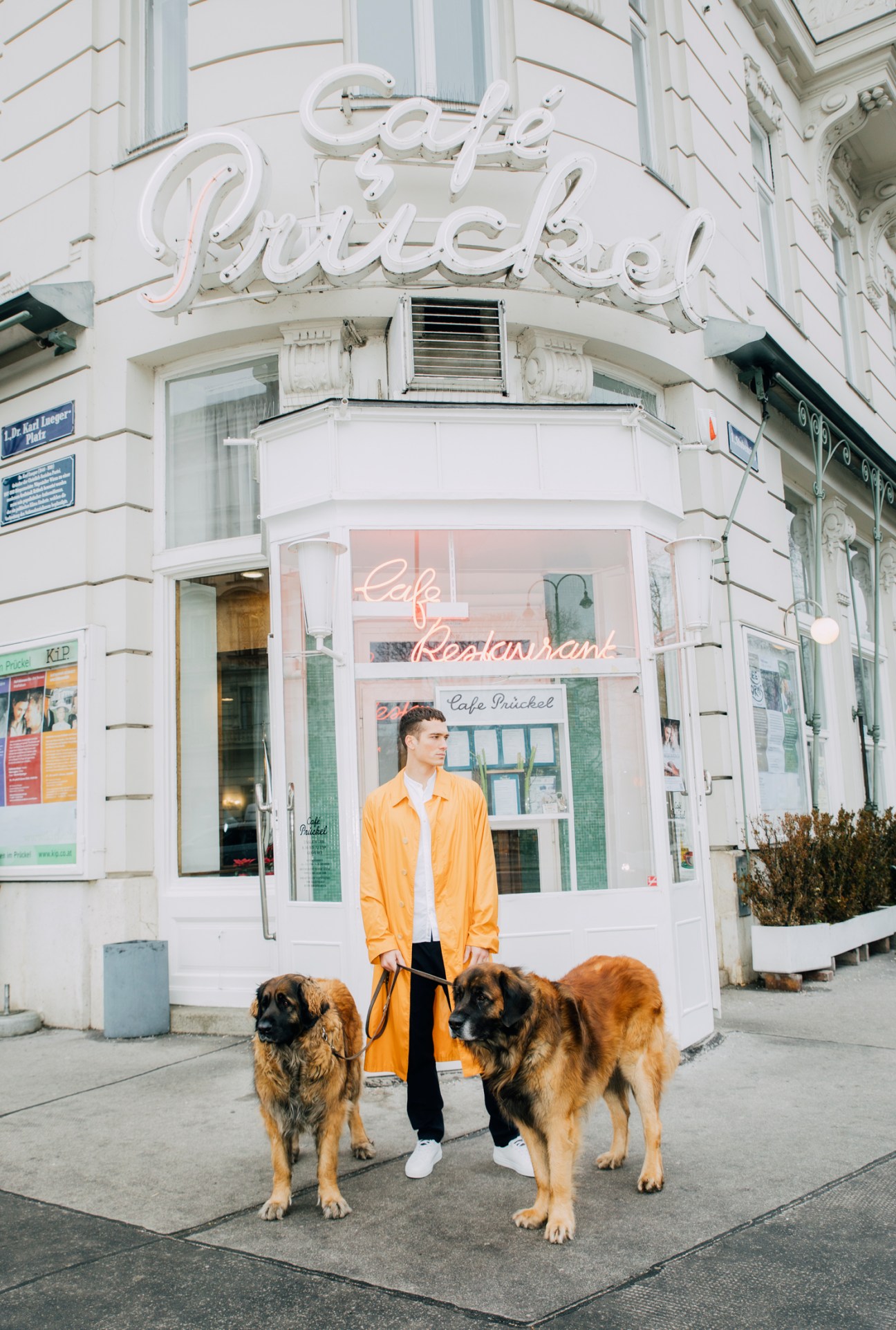 Man in yellow coat standing with two large dogs outside Cafe Prückel in Vienna