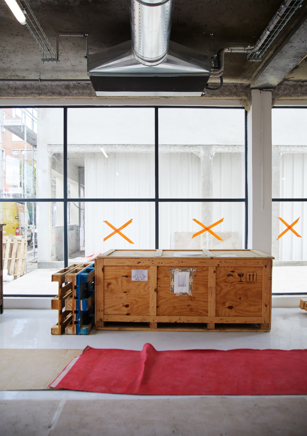 Large wooden shipping crates containing artwork sit in an industrial gallery space with concrete ceiling and windows