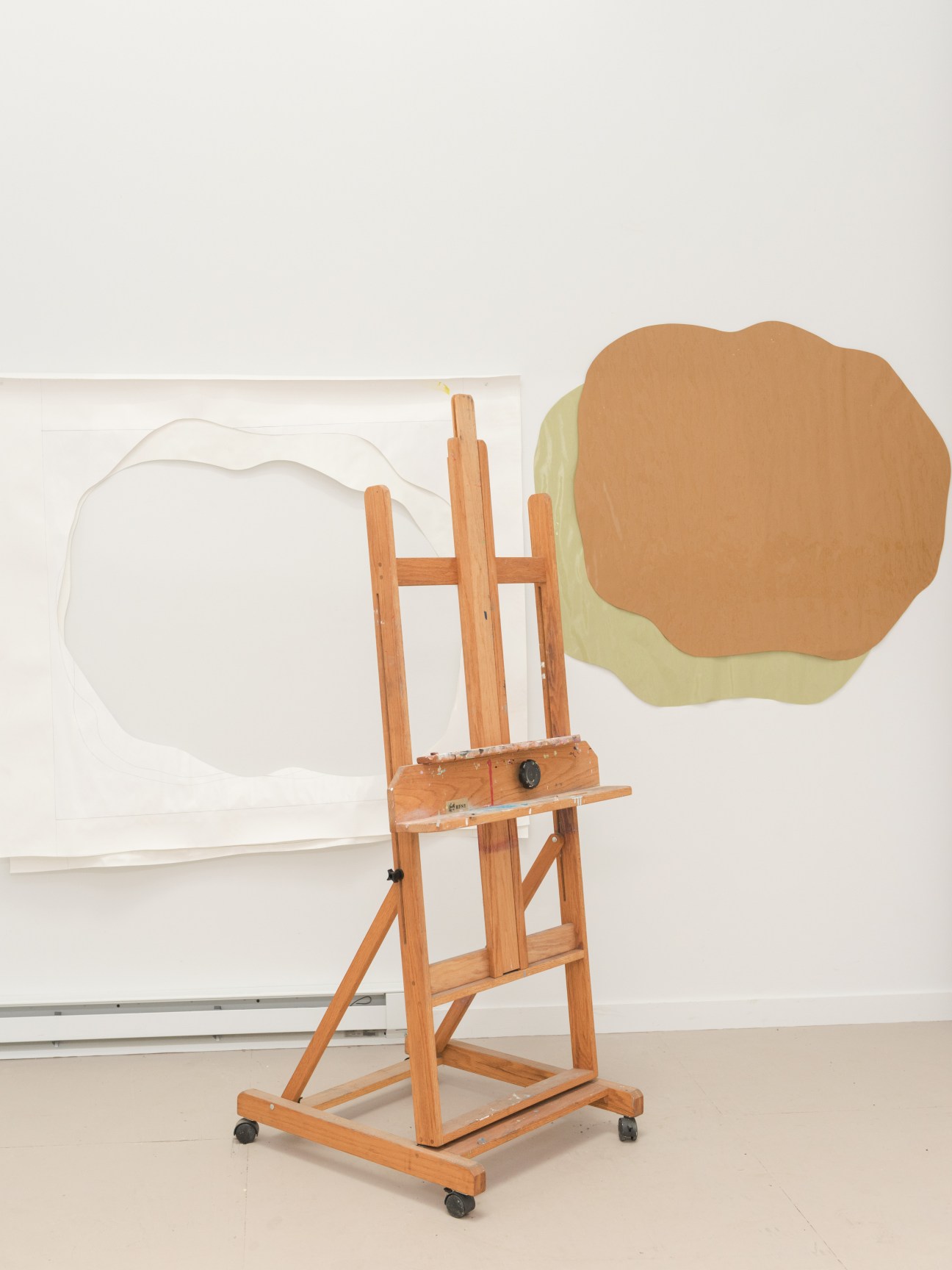 Wooden easel with abstract paintings on paper featuring organic shapes in tan and pale yellow tones.