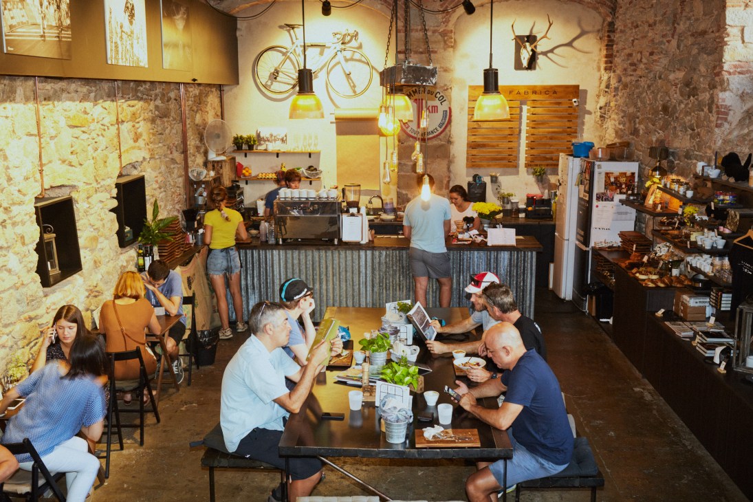 Interior of La Fabrica cafe with exposed brick walls, pendant lighting, bicycle wall art, and customers dining