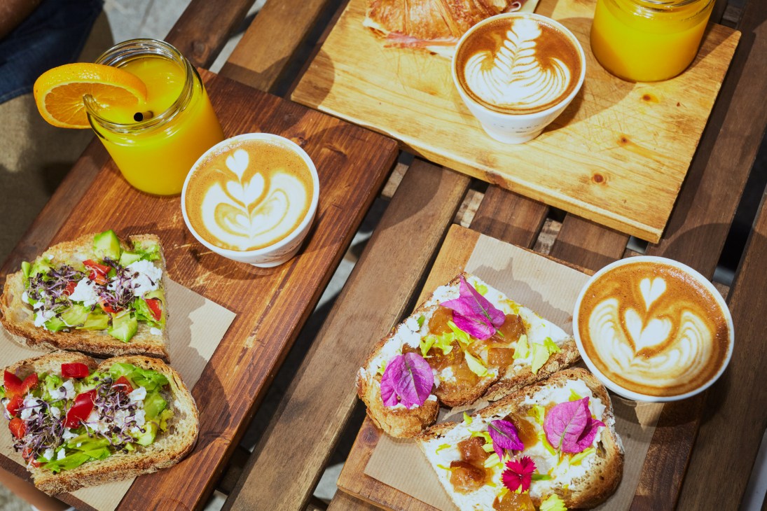 Breakfast spread at La Fabrica with avocado toast, coffee with latte art, and orange juice on wooden boards