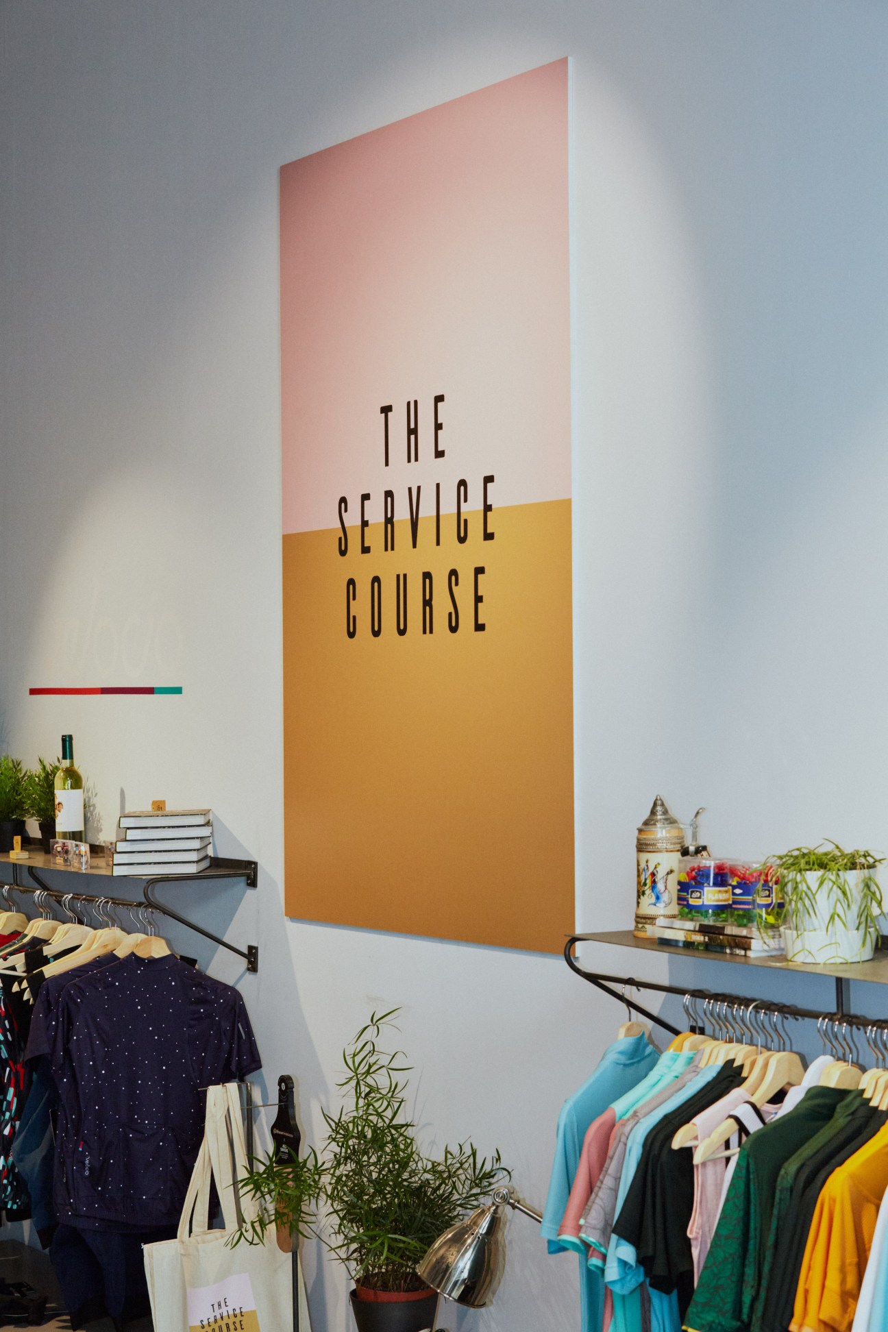 Interior of The Service Course cycling shop with clothing racks and large pink and orange wall sign