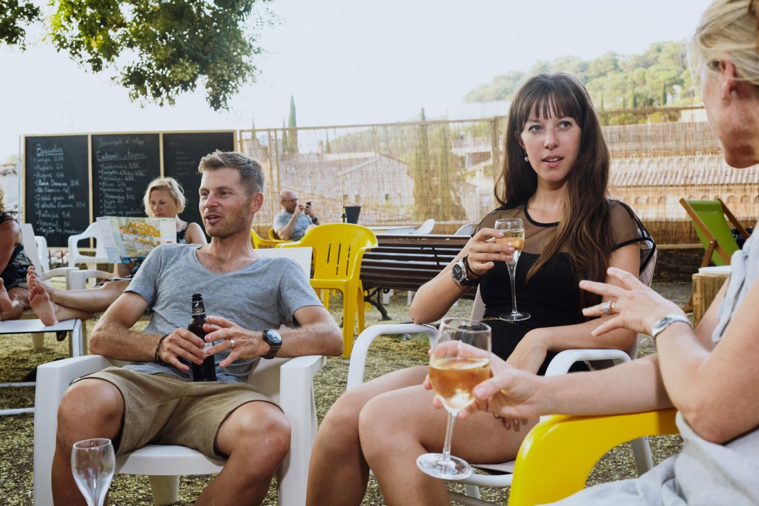Friends enjoying drinks and conversation at an outdoor terrace with white and yellow plastic chairs