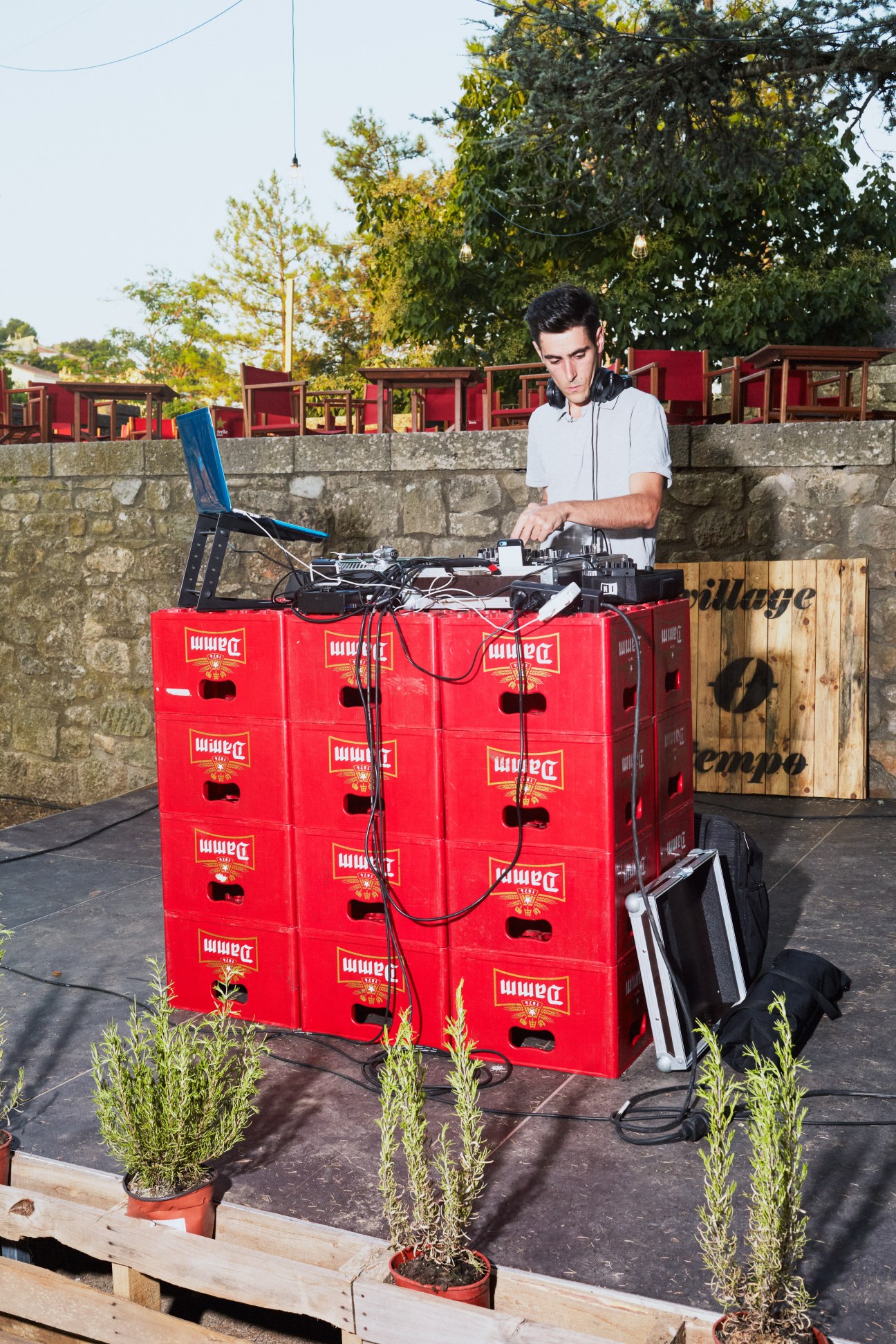 DJ performing with headphones and mixing equipment on stacked red beer crates outdoors at dusk