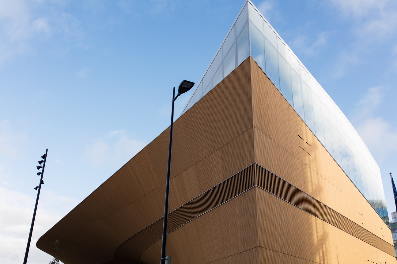 Modern Oodi Library building with curved wooden facade and glass upper section against blue sky.