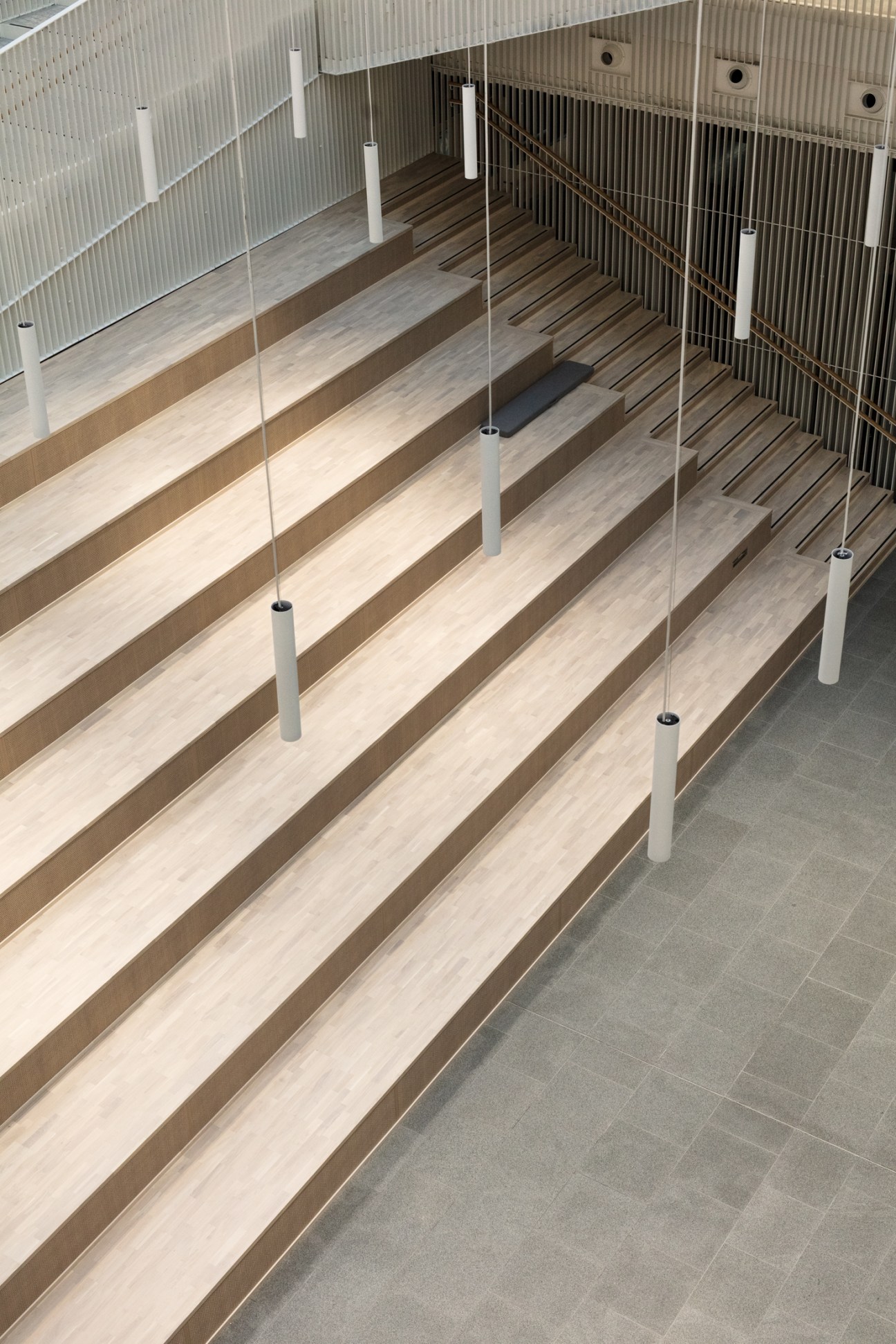 Interior atrium of Jätkäsaari School with wooden stepped seating, white railings, and metal supports.