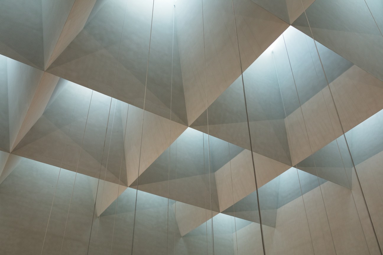 Geometric atrium ceiling with angular white panels and skylights creating a chevron pattern at Jätkäsaari School.