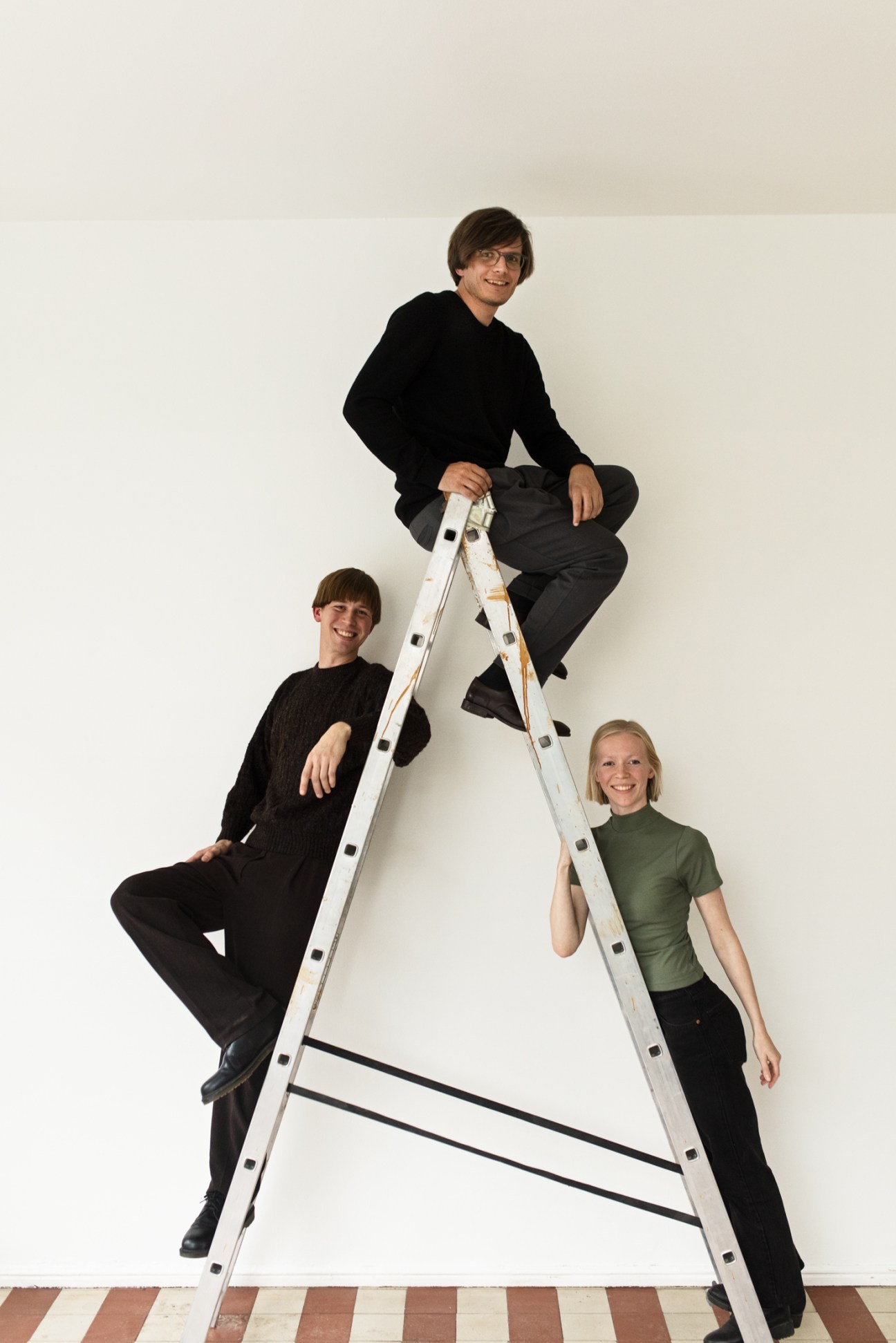 Three young architects pose on a ladder: Leo Lindroos, Antti Soini and Tuuli Kanerva from AS LL TK.