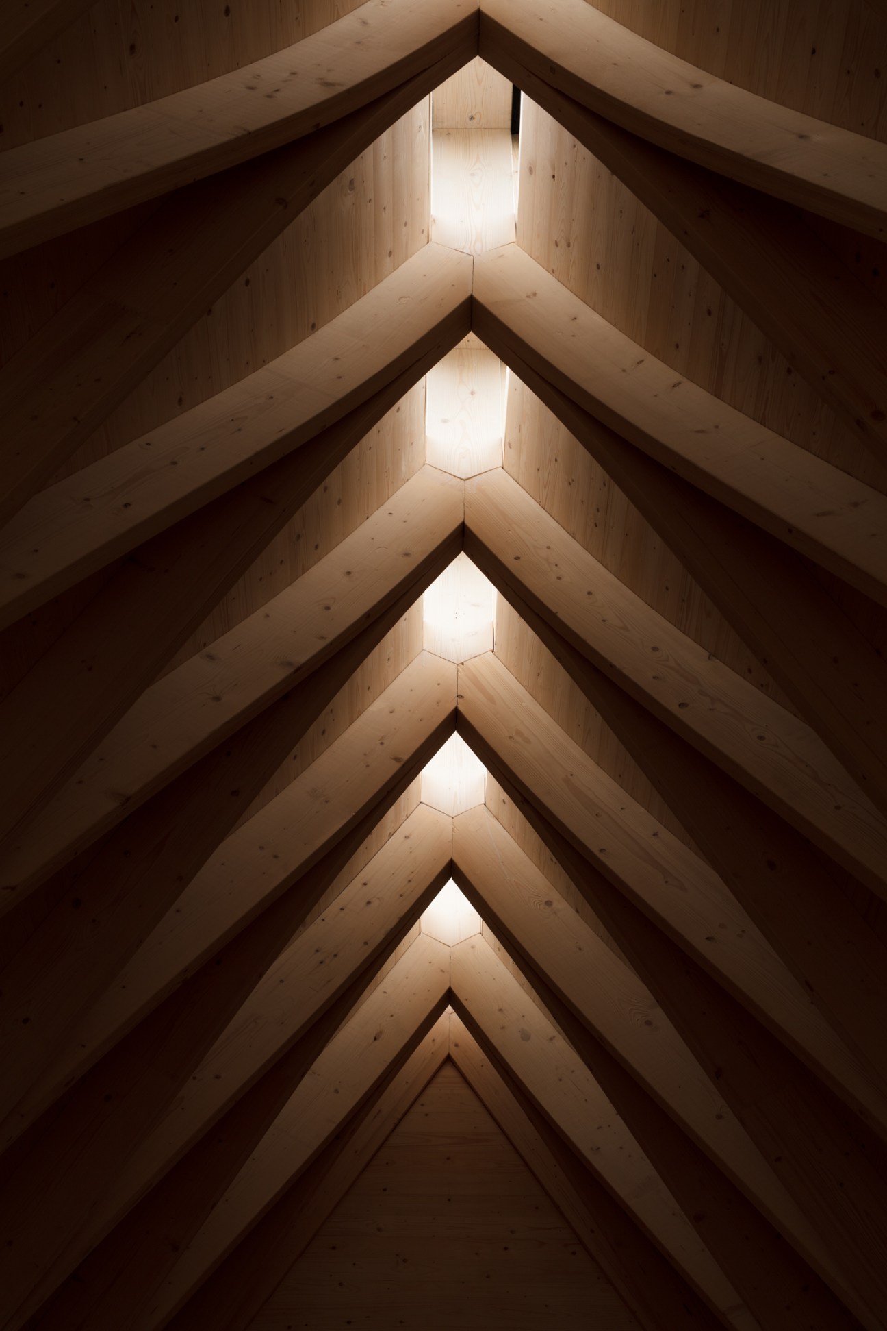 Symmetrical view of wooden spruce beams forming a vaulted ceiling with hexagonal skylights in Tervajärvi chapel.
