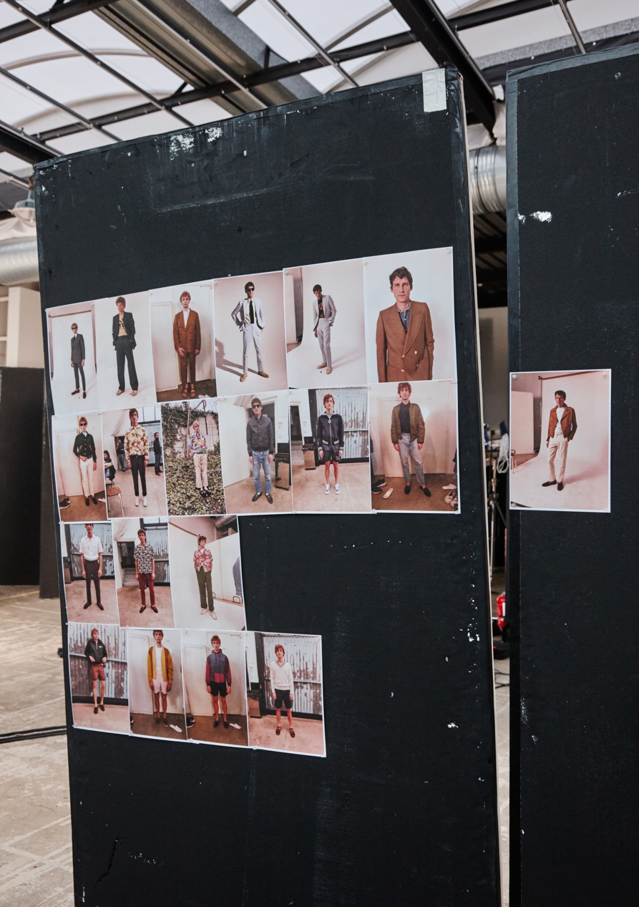 Multiple fashion photographs of male models in various casual and tailored outfits pinned to a black display board during a shoot.