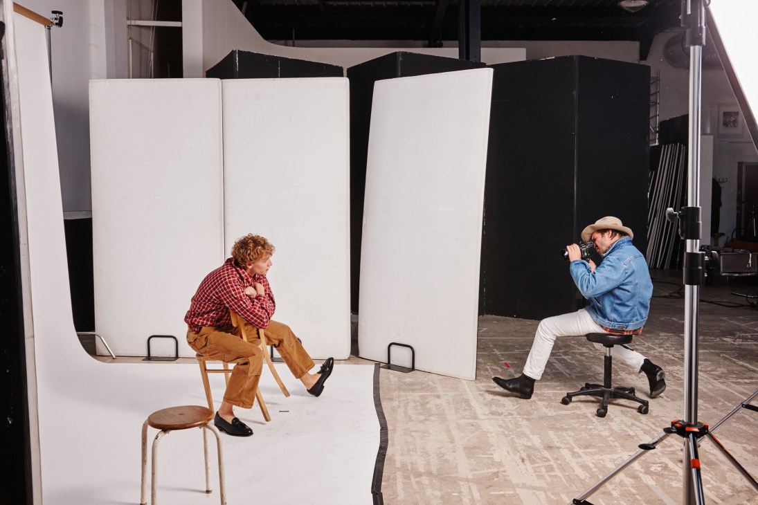 Photographer Sean Thomas shooting a male model wearing a red plaid shirt and tan trousers on a studio set.