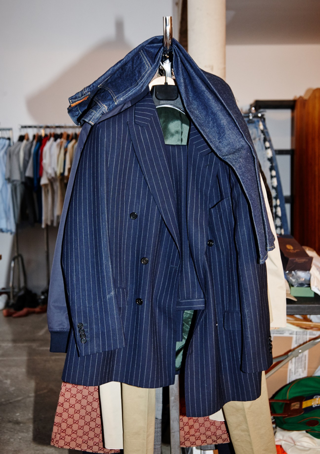Tailored pinstripe blazer draped over denim jacket on a hanger in a clothing studio.