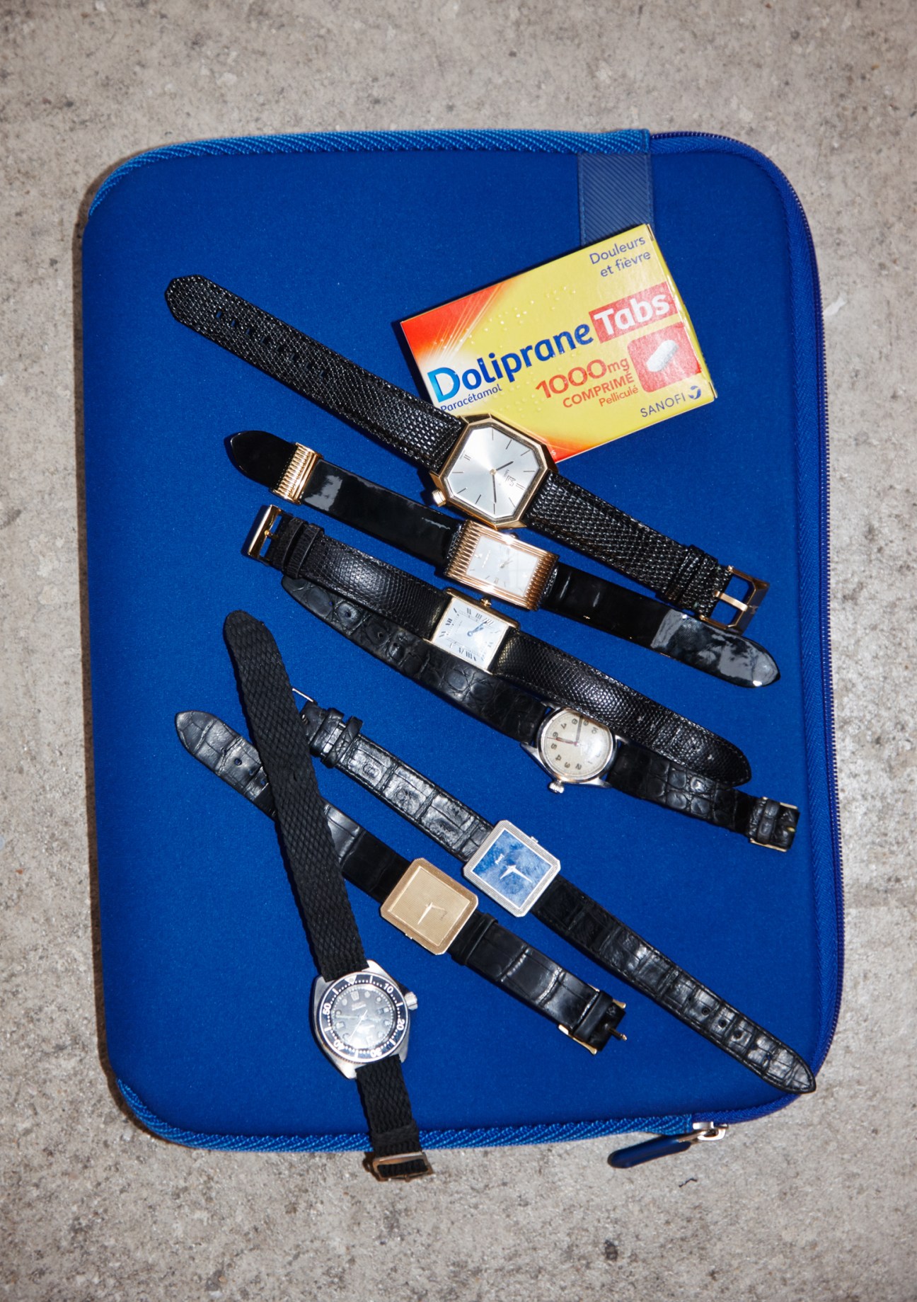 Collection of vintage watches and accessories arranged on blue laptop case with Dotiprone medication box.