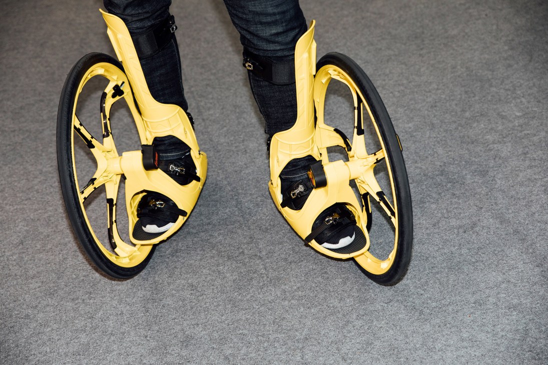 Person wearing bright yellow inline skates with black wheels and binding, shown from waist down on grey floor.