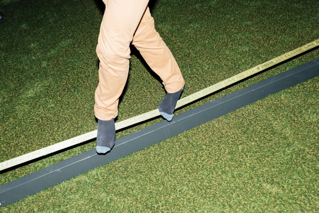 Person's legs in beige trousers and navy socks walking on a line across green turf.