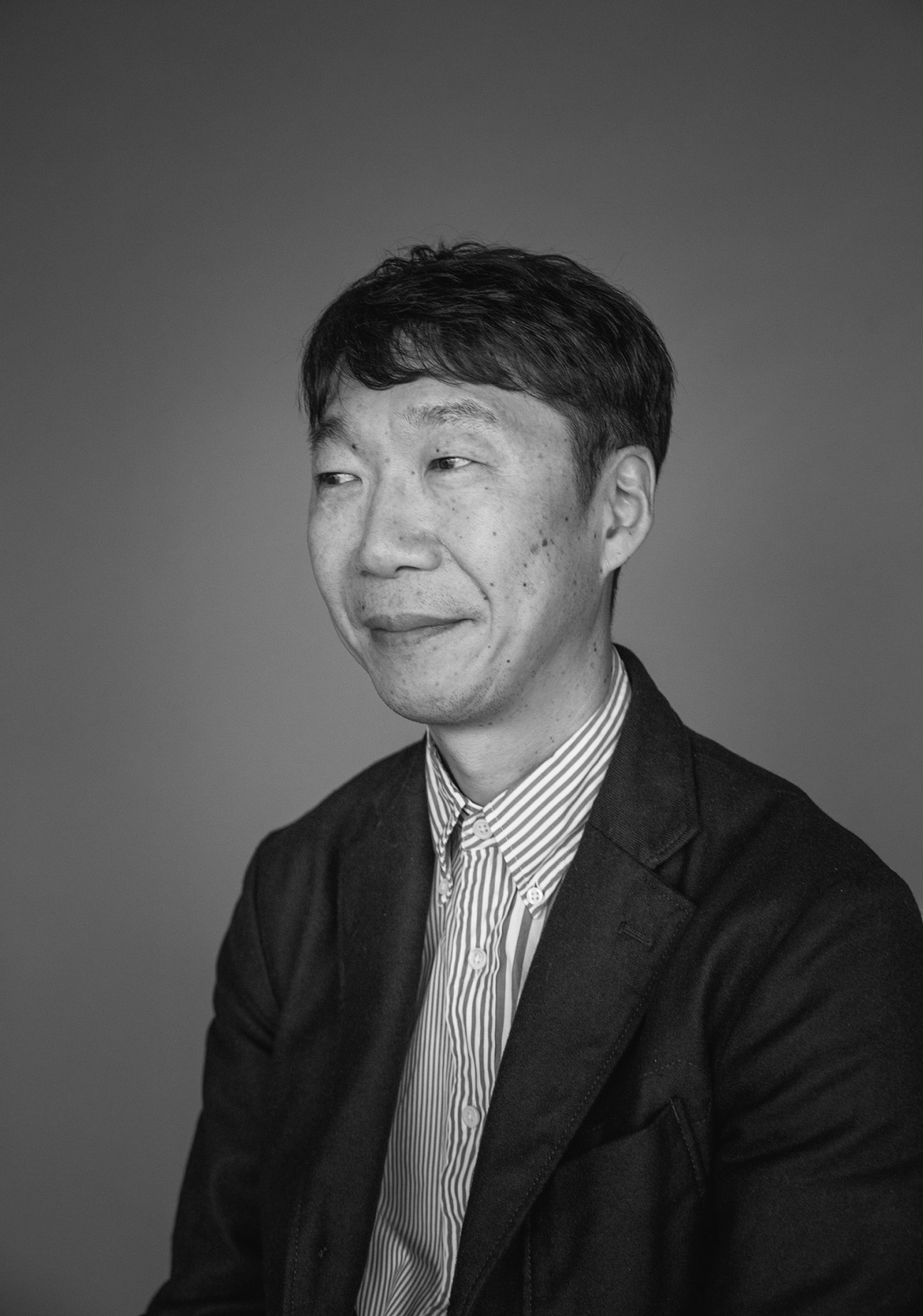 Portrait of Gen Arai, general manager at Goldwin, wearing a dark blazer and striped shirt.