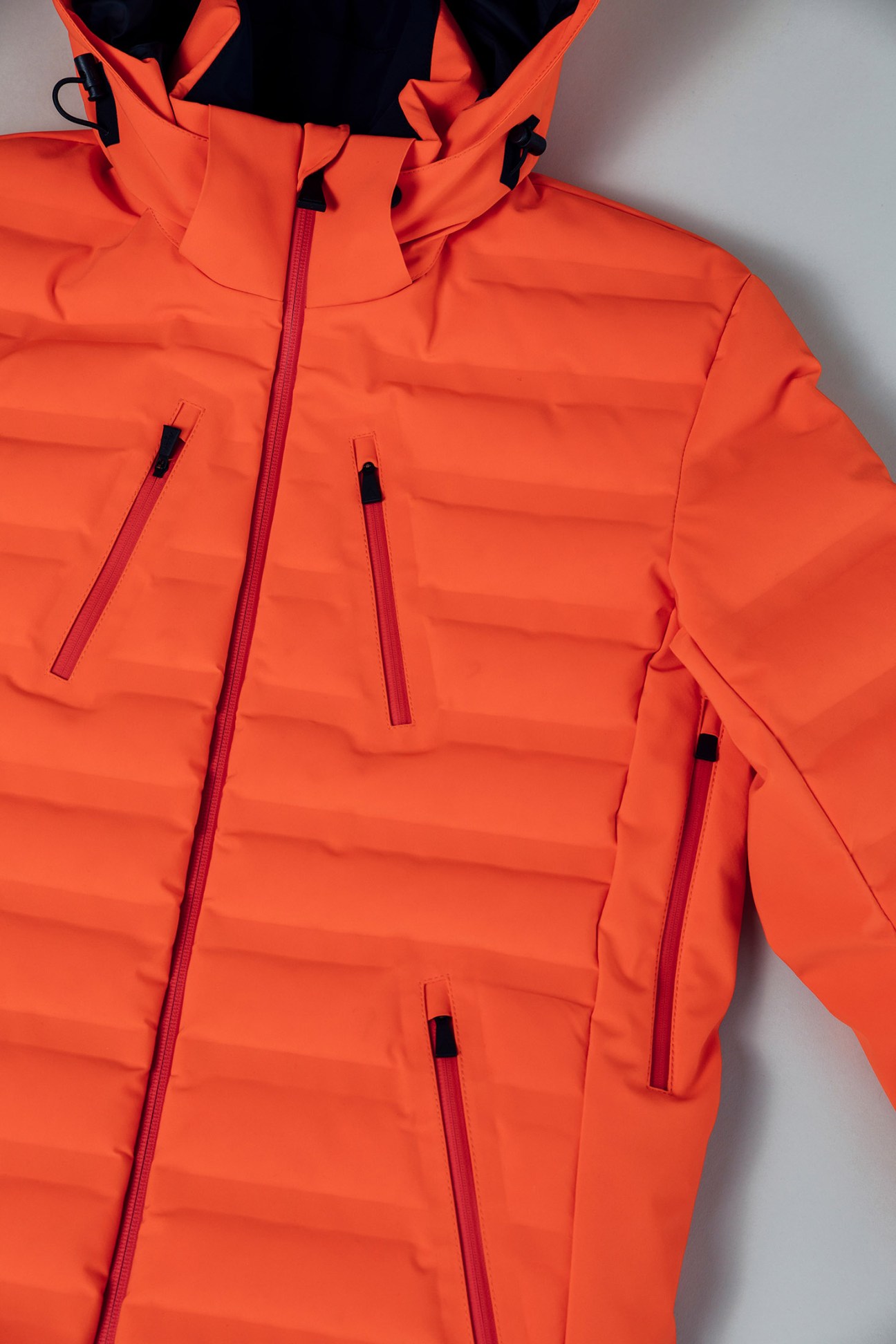 Close-up of a bright orange puffy jacket with burgundy zippers and black hardware details.