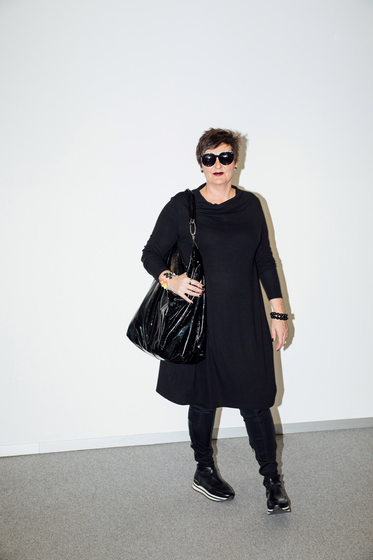 Woman wearing black dress, sunglasses, and carrying a black patent leather bag at Ispo sportswear fair.