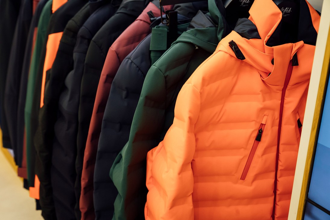 Row of colorful quilted puffer jackets displayed on hangers, featuring orange, black, burgundy, and green Aztech Mountain styles.