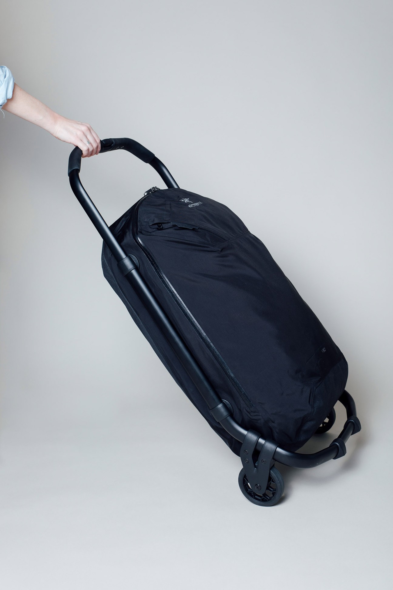Black Arc'teryx suitcase held by a hand wearing a light blue shirt sleeve.