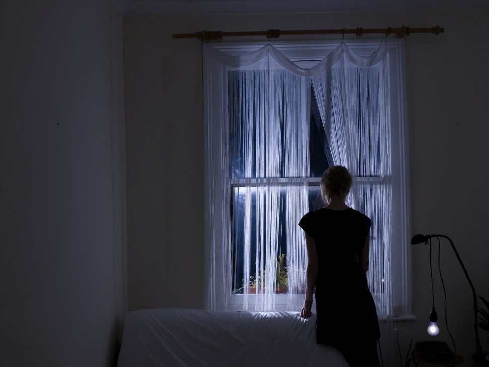 Artist Katie Paterson stands before a window with sheer curtains, silhouetted against moonlight streaming through glass.