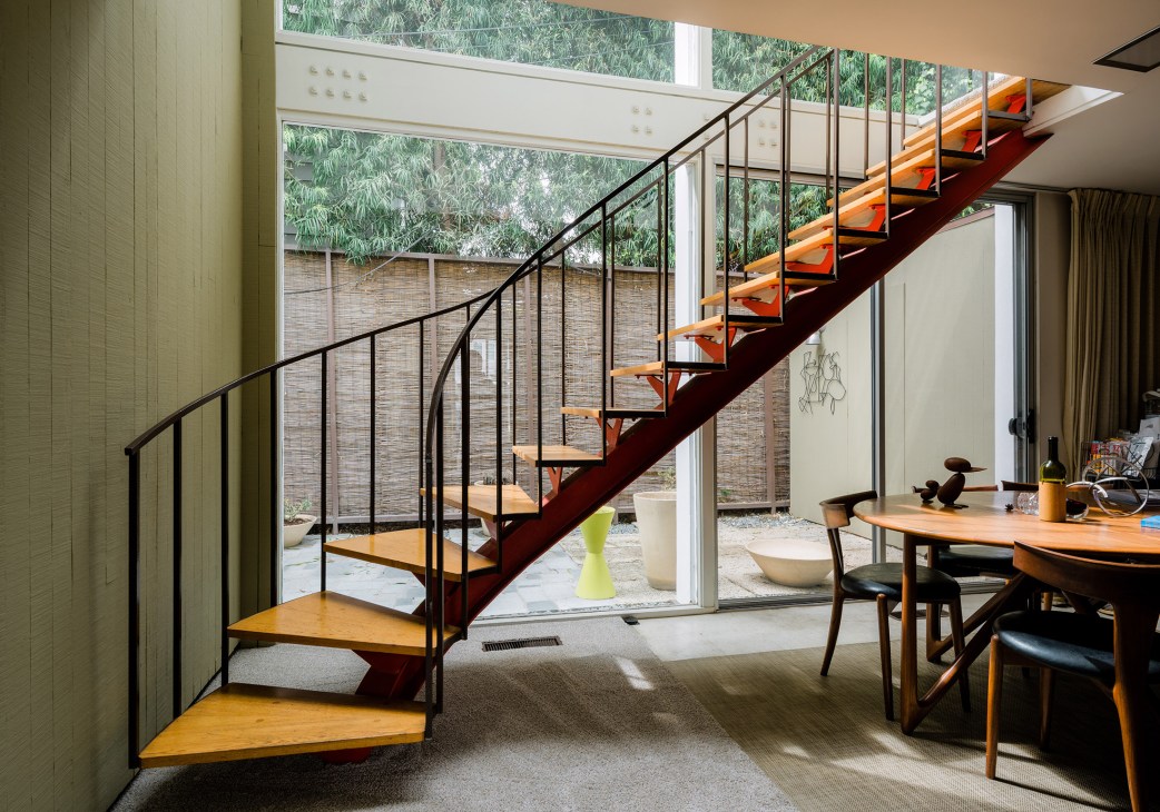 Mid-century modern interior with a curved metal bannister staircase and large windows overlooking a courtyard.