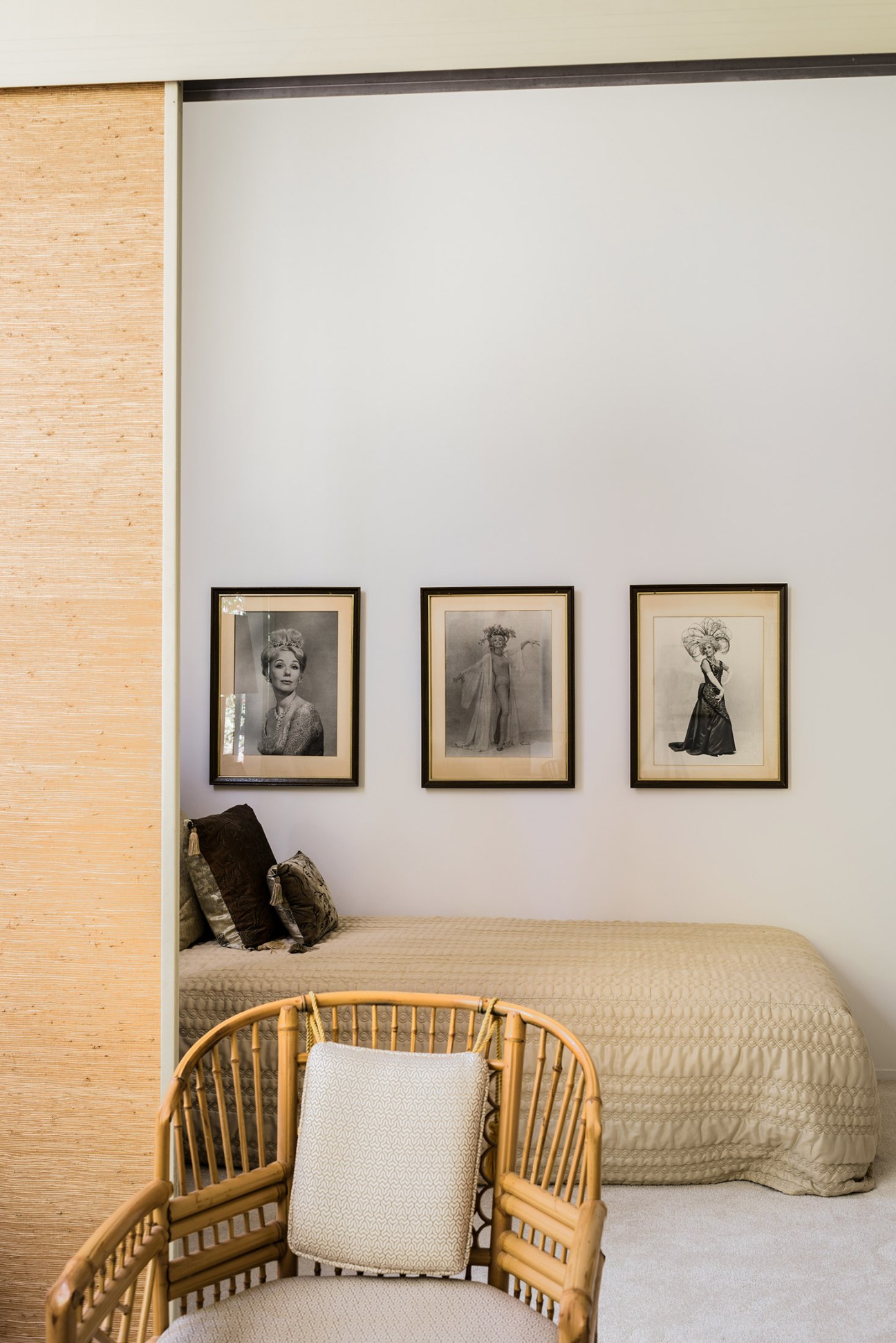 Bedroom with three framed black and white photographs of a woman in theatrical costumes hanging above a bed with woven headboard.