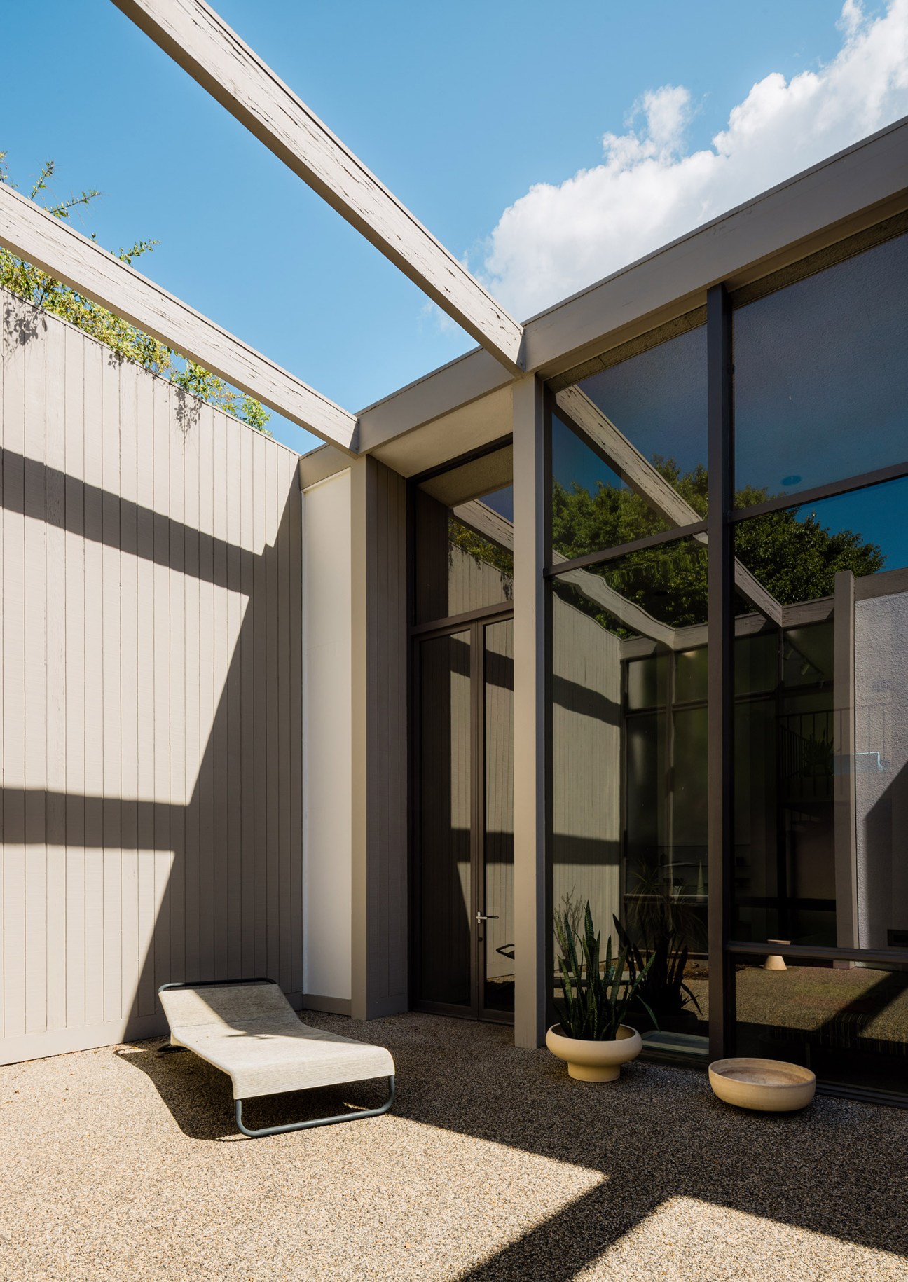 Modern mid-century patio with glass doors, wooden beams, and lounge chair overlooking landscaped courtyard.