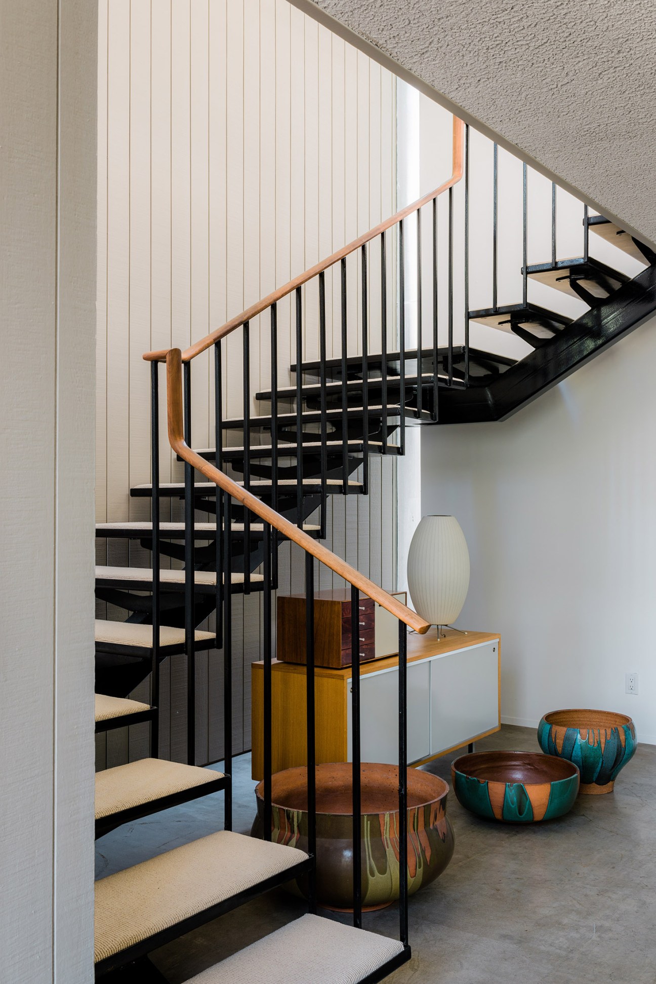 Mid-century modern staircase with black metal steps, wooden handrail, and vertical metal railings in the Brady House designed by Ed Killingsworth.