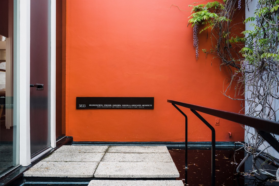 Orange-painted exterior wall of Killingsworth's former architectural practice building with a plaque identifying the firm.