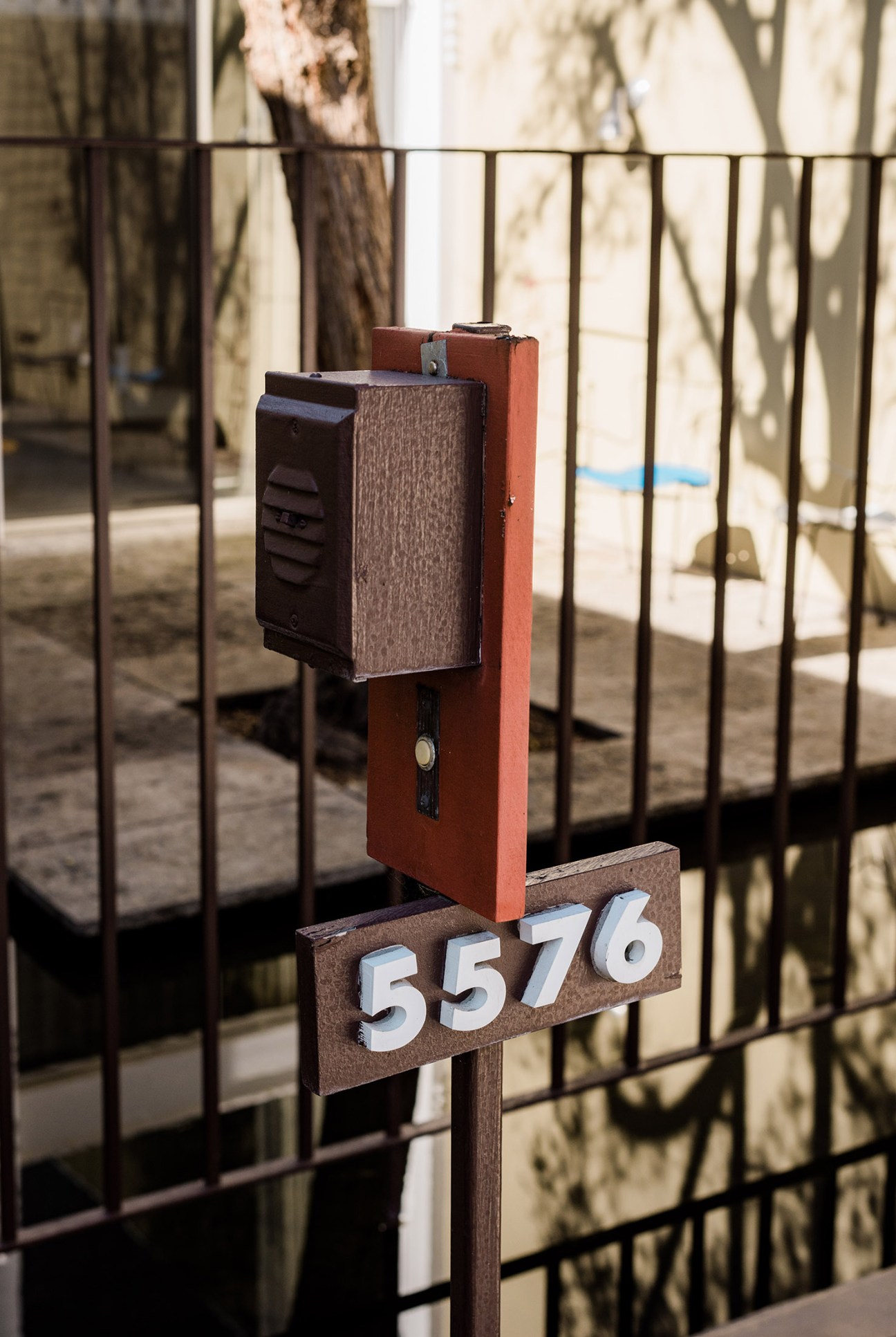 A mid-century modern mailbox with coral-red frame and dark wood accents mounted on a gate, displaying the house number 5576.