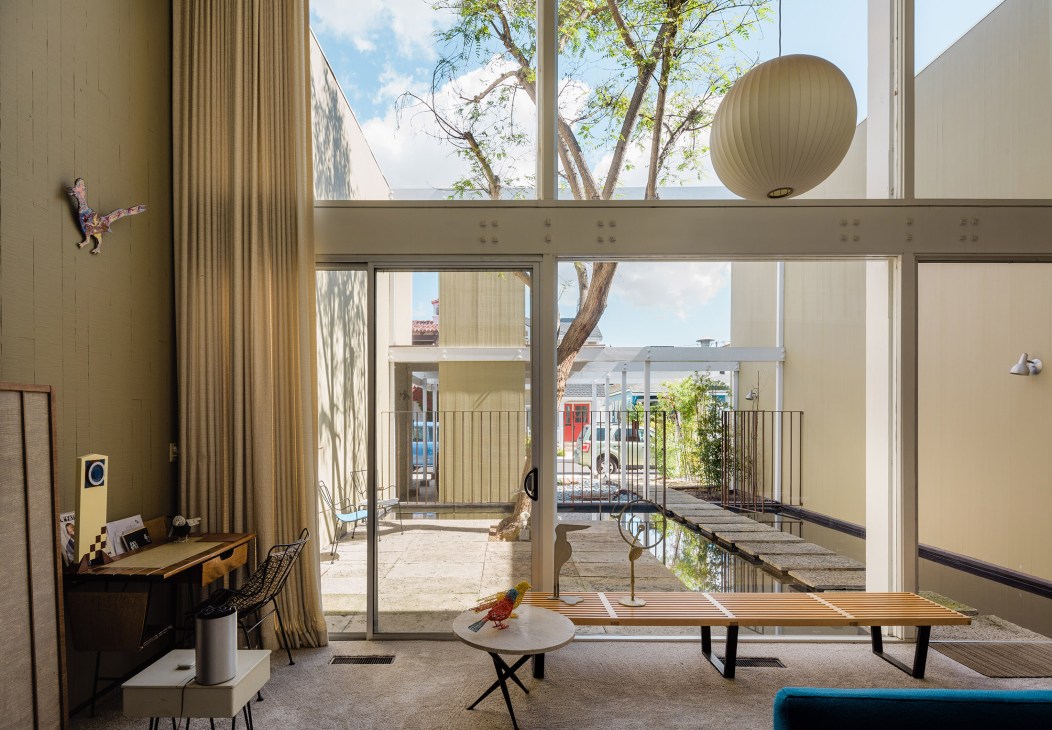 Mid-century modern interior with floor-to-ceiling windows overlooking a courtyard water feature and olive trees.