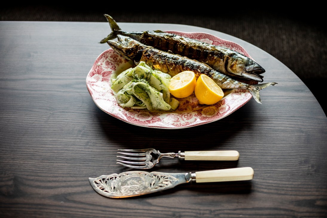 Roasted mackerel with fennel and lemon on a pink patterned plate with silver cutlery.