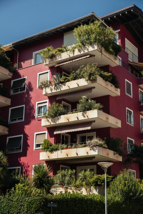 Red residential building with cream balconies and potted plants in Locarno