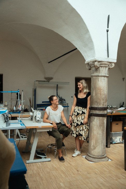 Two women in a design studio with sewing equipment and a classical stone column.