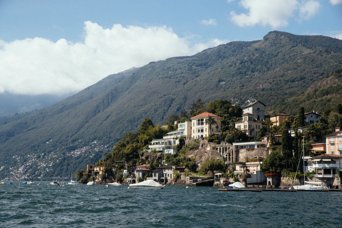 Waterfront buildings nestled against forested mountainside along Lake Maggiore in Locarno, Switzerland.