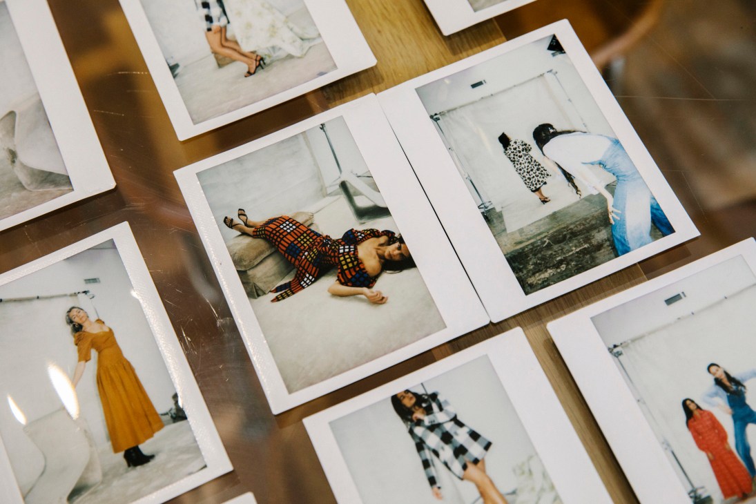 Polaroid photographs of models wearing various dresses and outfits arranged on a wooden surface.