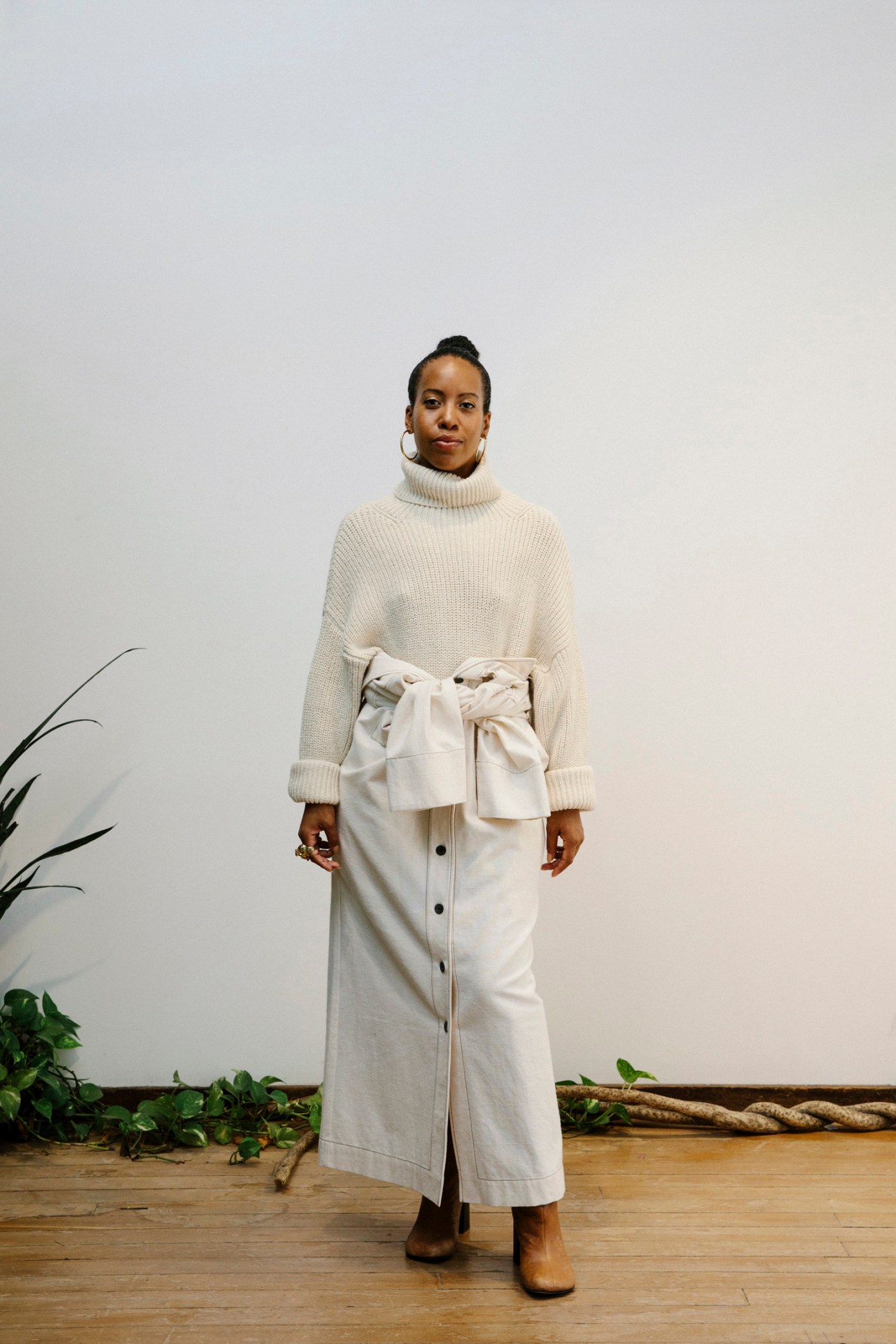 Woman wearing a cream turtleneck sweater and white button-front midi skirt with tied waist detail.