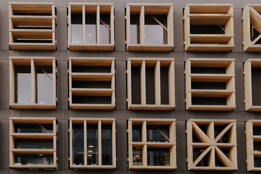 Modern building façade with wooden window frames and white panels on grey exterior wall.