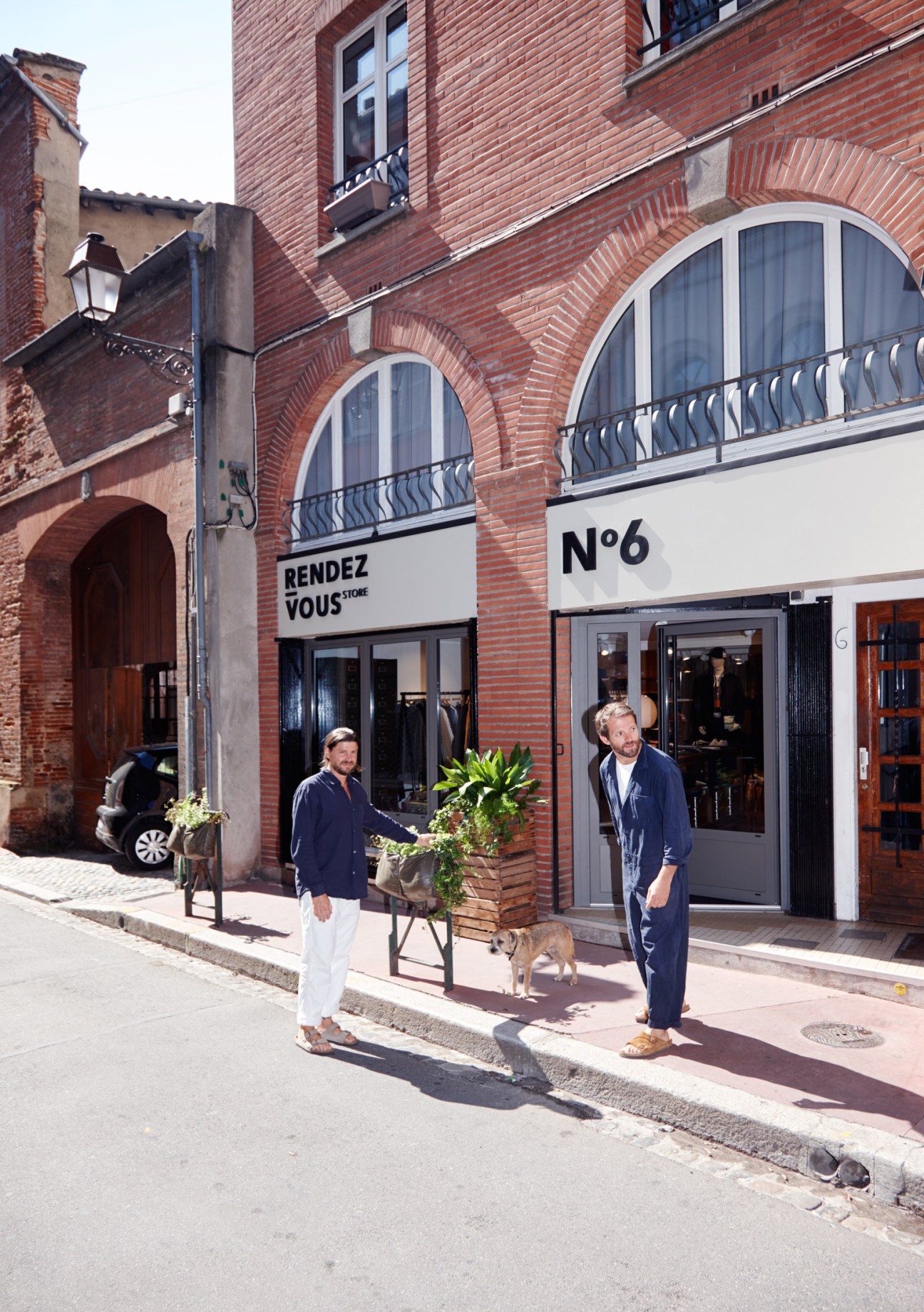 Marc Llorens and Olivier Salette standing outside Rendez-Vous menswear shop in Toulouse with their dog.