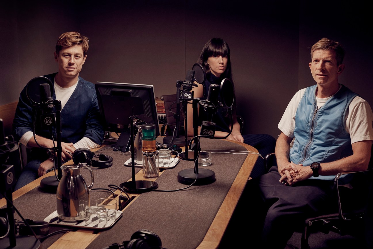 Three people sit at a table in a radio studio with microphones and equipment during a roundtable discussion about fashion.