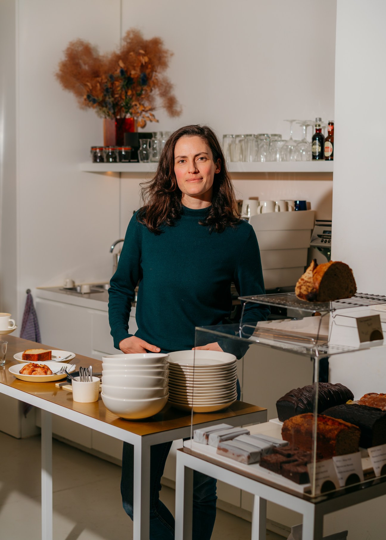 Ruth Barry stands in her Berlin bakery behind a counter displaying bread, cakes, and stacked plates