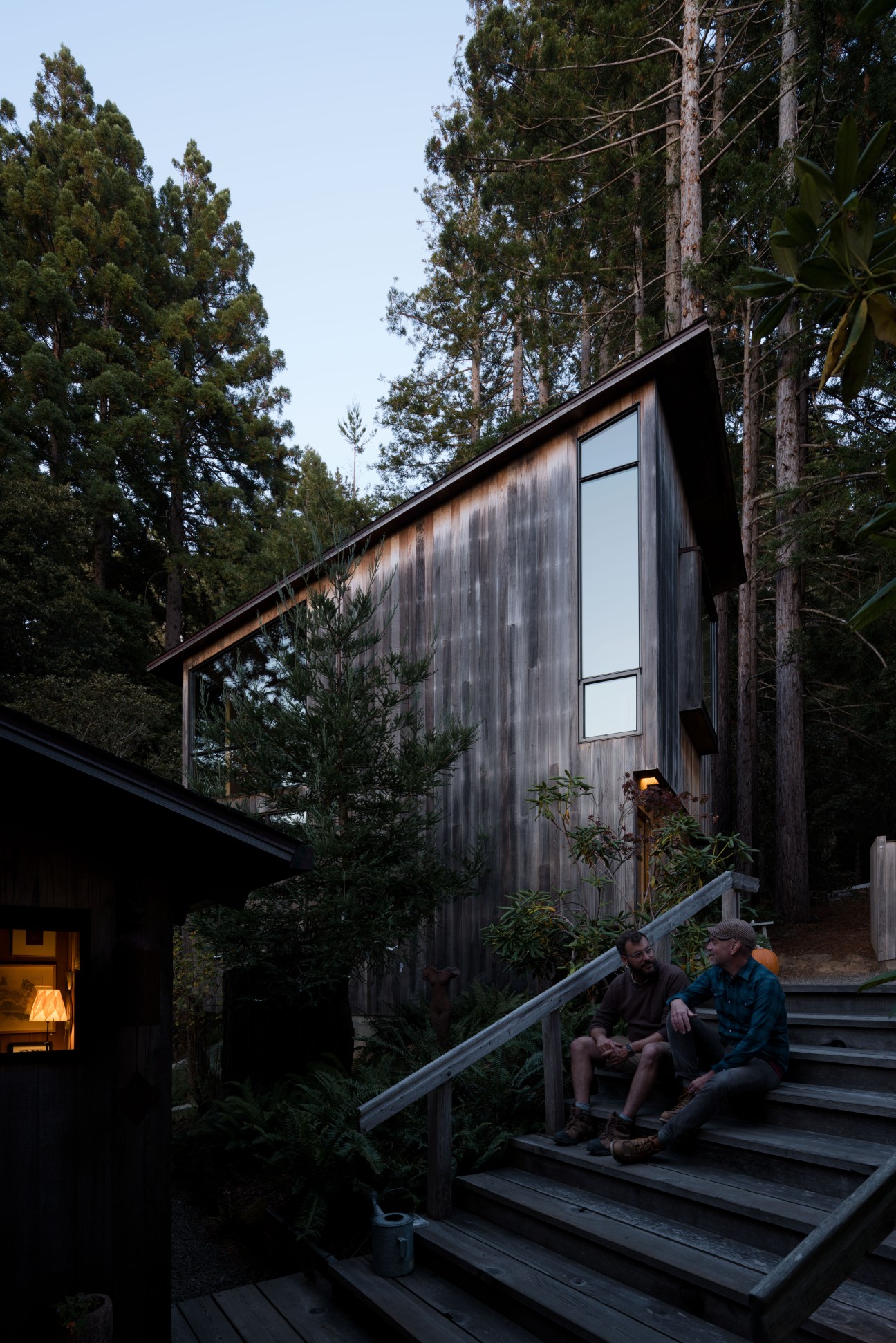 Peter Jenny's wooden Sea Ranch home with modern extension, two people sitting on the deck at dusk.