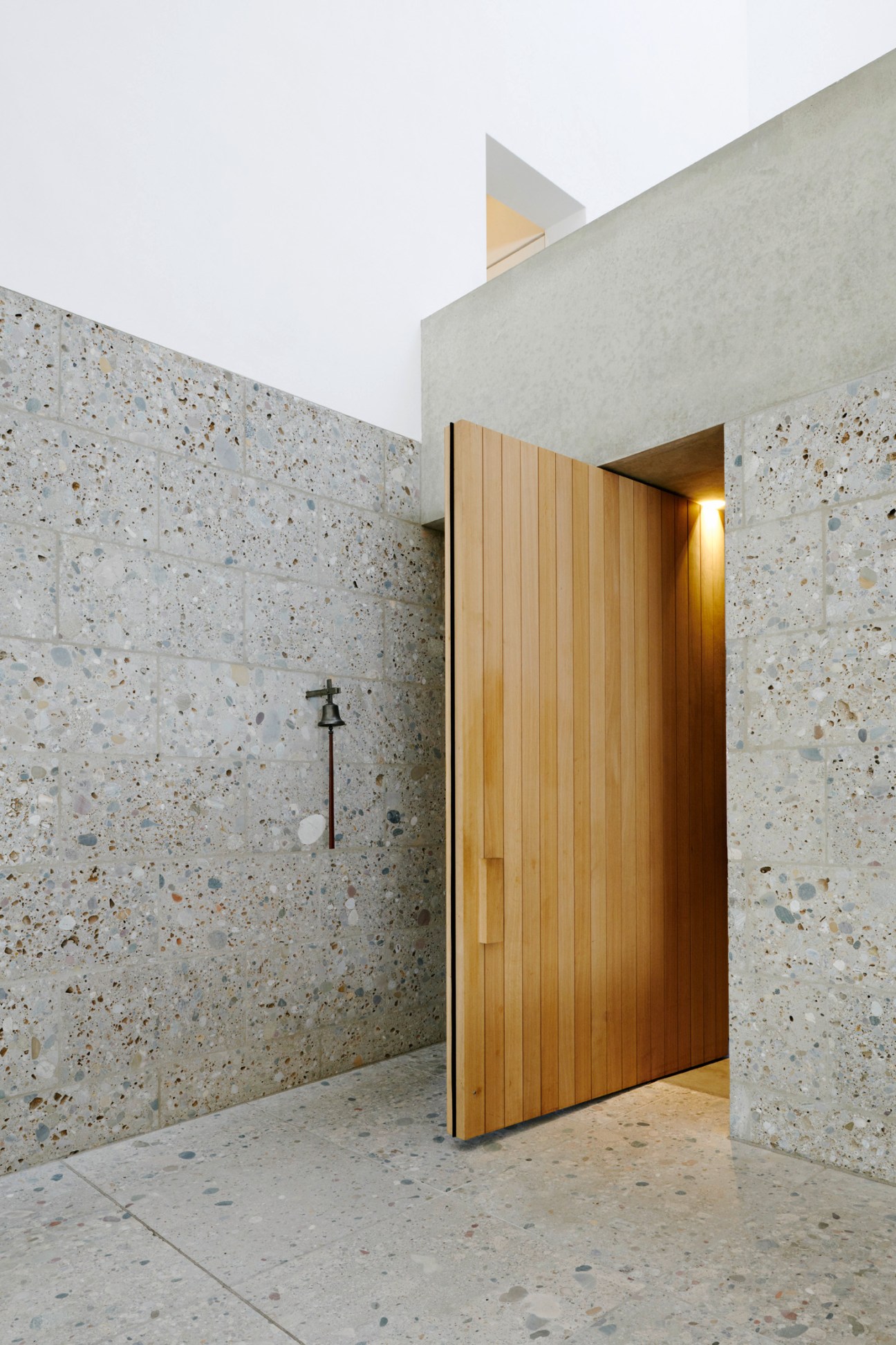 Interior of Church of the Blessed Father Rupert Mayer showing a wooden door and cross against terrazzo stone walls.