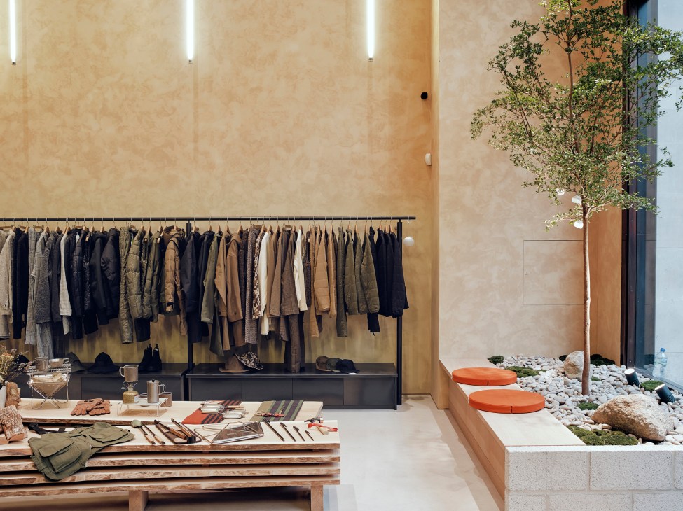 Snow Peak London store interior with warm wood walls, clothing racks, display table, and indoor tree garden area